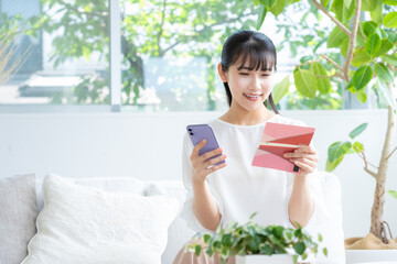 リビングで通帳とスマホを見る若い女性