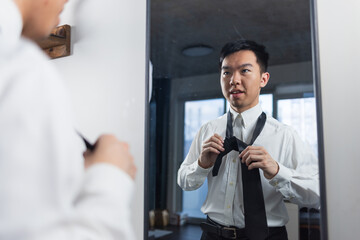 A young man looks into the mirror while adjusting his tie with focus. The scene suggests confidence, preparation, and professional ambition.