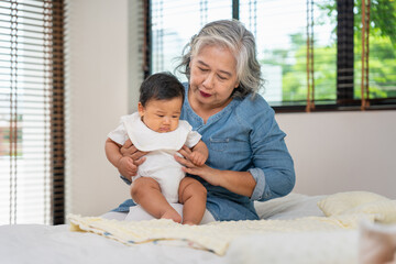 Loving Grandmother Comforting Crying Baby, Grandparent Holding Grandchild on Bed at Home, Asian...