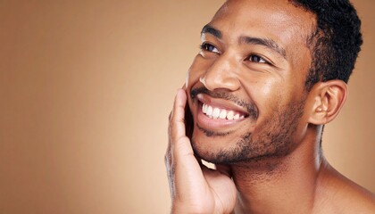 Obraz premium Happy young man with healthy skin, smiling and touching his face, looking thoughtfully upward.