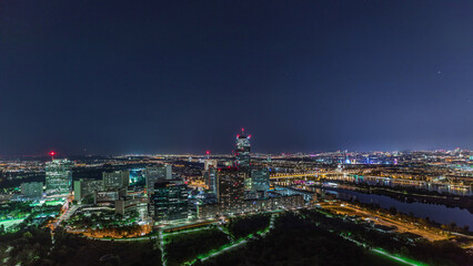Aerial panoramic view over Vienna city with skyscrapers, historic buildings and a riverside promenade night timelapse in Austria.