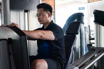 Man exercising on a fitness machine in a gym during the day while wearing glasses and a black shirt