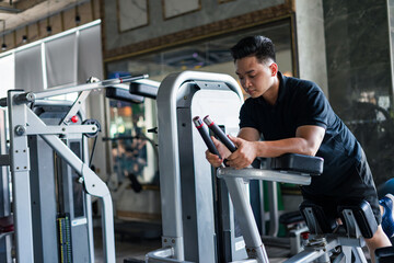 Young Asian man engaged in strength training at a well-equipped gym during the afternoon hours