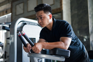 Young Asian man engaging in strength training at a gym focused on fitness and muscle building...