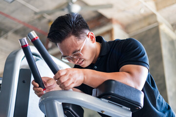 Focused Asian man exercising on a gym machine in an industrial-style fitness center during the...