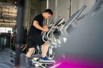 Young man exercises on an elliptical machine in a modern gym during the morning hours focusing on fitness and health improvement