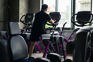 Individual exercising on elliptical trainer in modern gym with large windows showing outdoor view...