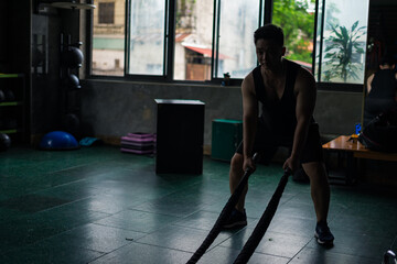 Fitness enthusiast training with battle ropes in an urban gym during morning hours, focusing on...