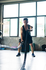 Obraz premium Young Asian man exercises with battle ropes in a modern gym during daytime for strength training and fitness
