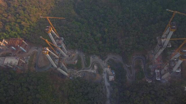 Industrial crane towers in expressway road construction site, Sahyadri mountains and forest, Mumbai Pune Expressway construction site, Lonavala, Maharashtra, Establishing drone shot