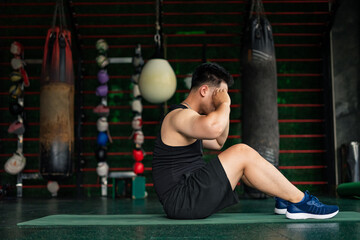 Man performs sit-up exercise in a gym with punching bags and fitness equipment during workout...