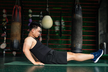 Asian man performs bodyweight exercise on gym mat in training area during daylight focused on...