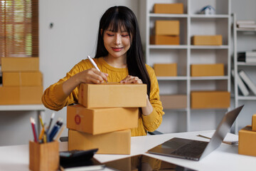 
Young woman small business owner writing on parcel box preparing package product fos her customer....