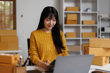 Startup small business, A young Asian woman checking online order on laptop and packing boxes for...