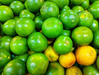 Pile of Fresh Green Oranges. Vibrant Citrus Fruits Background. Green and Yellow Oranges at a Market. Fresh Tangerines for Sale. Close-up of Unripe Citrus Fruits