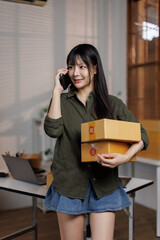 Asian Young Female entrepreneur using mobile phone and preparing orders for shipping in a...