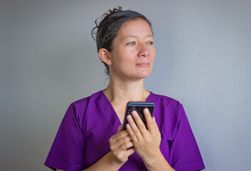 Female doctor wearing purple scrubs holding smartphone and looking away