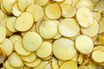 Pile of potato slices submerged in water. Potato slices background. Carbohydrate foods. Top view