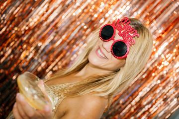 Woman wearing festive glasses and holding a drink celebrating new year's eve