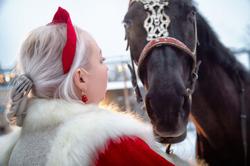 Beautiful Russian girl in national dress poses with horse during Maslenitsa holiday celebration