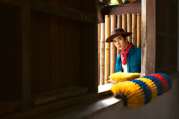 Handsome young cowboy in blue jeans shirt and cowboy hat in barn