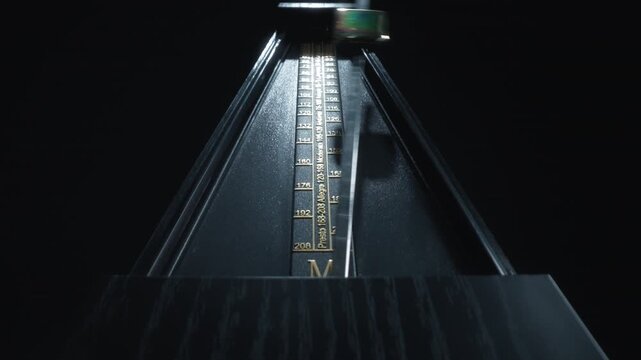Dolly shot of an old-fashioned black metronome swinging back and forth