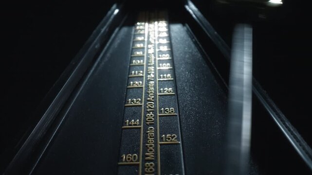 Dolly shot of a vintage black metronome swinging back and forth
