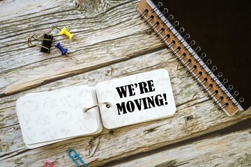 WE'RE MOVING! on a small notebook on a wooden table. image from above.