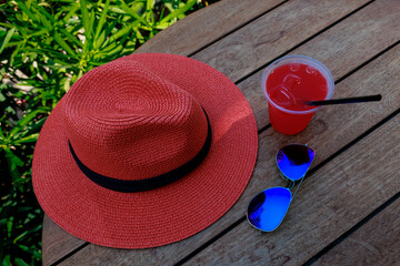 Glass of refreshing cocktail with sunglasses, straw hat on wooden table against blue sky and...