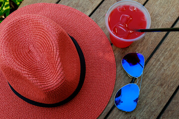 Glass of refreshing cocktail with sunglasses, straw hat on wooden table against blue sky and...