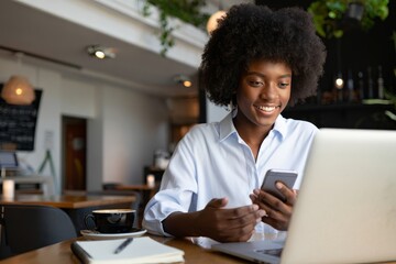 African american woman using smartphone and laptop in cafe for remote work study