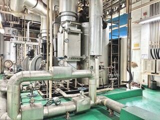 Interior of an industrial plant with stainless steel tanks, pipelines, and mechanical equipment. Clean green flooring contrasts with complex process engineering infrastructure in operation