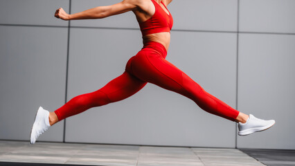 Dynamic Woman in Red Workout Gear - Jump Shot, A full-length action shot of a woman in a vibrant red sports bra and leggings, captured mid-air in a dynamic jump. She's wearing white sneakers.