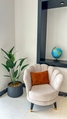 Modern Lounge Corner With Beige Armchair, Orange Cushion, Potted Plant, And Globe On Shelf, Indoor Daylight, Minimalist Interior, Ideal For Real Estate, Home Decor, Lifestyle Branding, Editorial Use