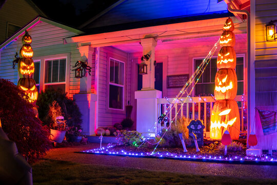 Halloween house decorations with orange lights, glow garlands and pyramid of pumpkins. Illuminated night decor