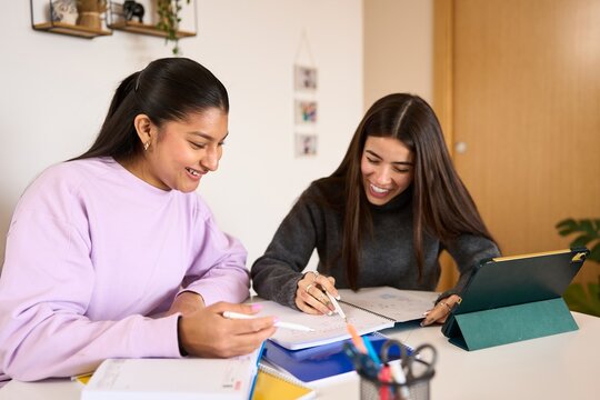 Two happy students studying together with a digital tablet and notebooks, smiling and collaborating on their homework