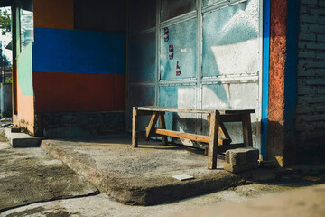 Abandoned Urban Space: Weathered Wooden Bench and Textured Walls Under Bright Sunlight