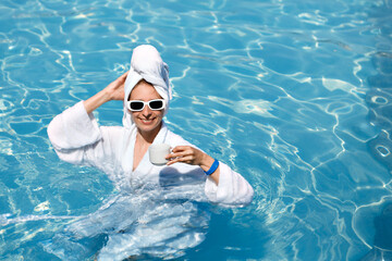 A girl in a white coat swims in a blue pool. Wearing sunglasses and a towel. Epilation of legs,...