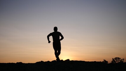 Silhouette Runner Against Sunset Sky: A lone runner is silhouetted against a gradient sunset,...
