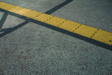 Yellow Tactile Paving Strip on Textured Asphalt with Angular Shadows: Urban Accessibility and...