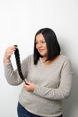 An adult Latina woman shows off the braid of hair she cut to donate for oncological wigs for girls...