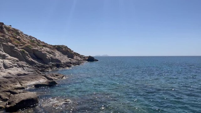 Scenic footage of waves hitting rocky shoreline at Kalafati Beach, Mykonos. Clear blue Aegean Sea, natural coastal beauty, and a serene Mediterranean setting.
