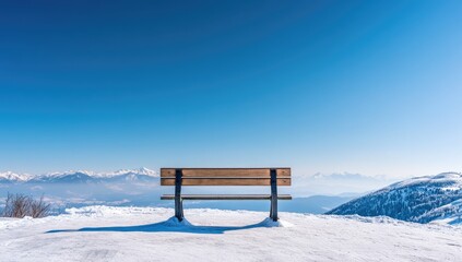Empty wooden bench on snowy mountaintop, clear blue sky
