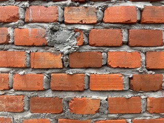 Textured close-up of a rustic red brick wall with cement mortar.