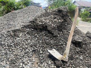 A close-up of a shovel resting on a mound of gravel in a construction site.