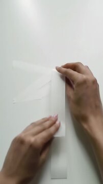 Well-manicured hands place matte white tape on pristine studio tabletop forming geometric patterns in high-key setting with dolly zoom, ECU videos, concept of strategic problem-solving.
