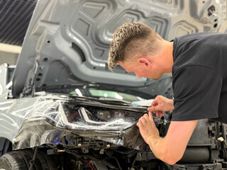 A car wrapping specialist applies a polyurethane film to the car. Detailer smoothes PPF. Car wrapping, detailing, tuning and styling. Selective focus. PPF protective film against chips and scratches. 