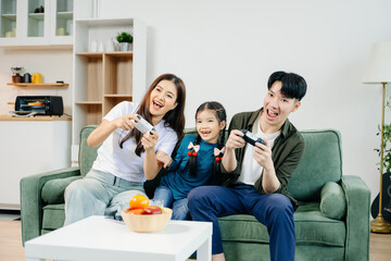 Happy Asian parents and child bonding, playing games, laughing, and enjoying social media together in cozy living room. Family time, love