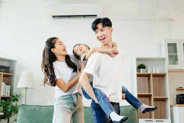 Asian parents and daughter enjoying a playful piggyback ride, laughing and bonding in cozy living...