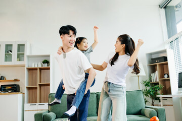 Asian parents and daughter enjoying a playful piggyback ride, laughing and bonding in cozy living...